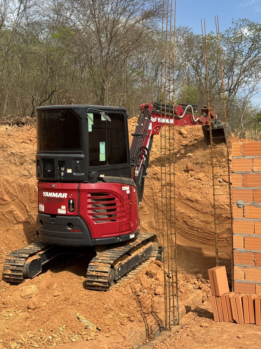 Mini escavadeira abrindo vala em obra com vergalhões